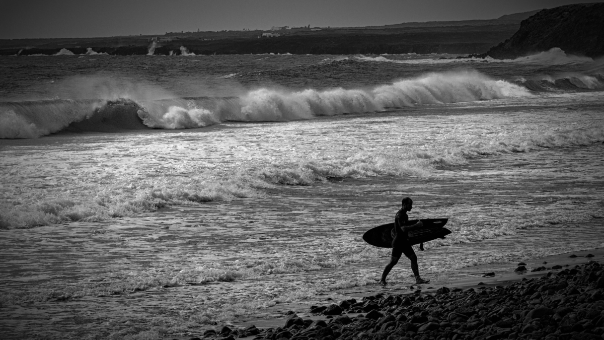 a surfer in silhouette coming out of the ocean with its massive waves in the background