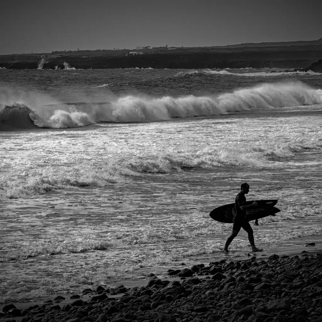 Black and white photo of a surfer getting out from the ocean and walking on the beach