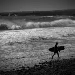 Black and white photo of a surfer getting out from the ocean and walking on the beach