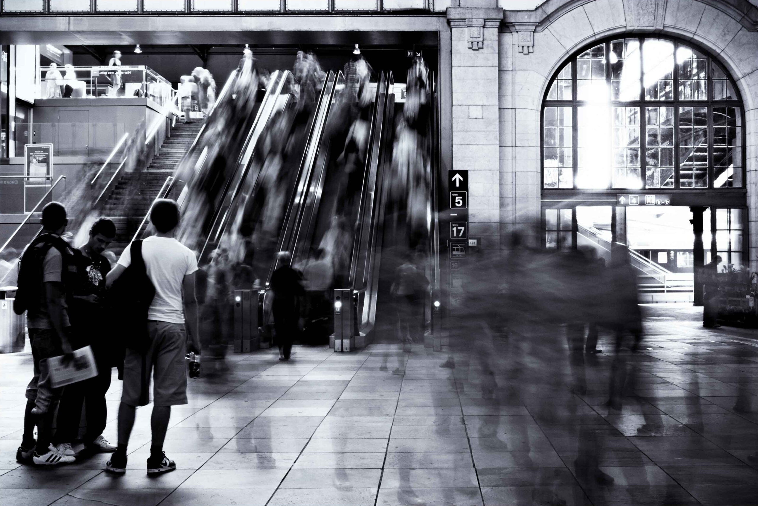 three stiil individuals close to a blurred flow of rushing people at a train station. Long exposure photo.