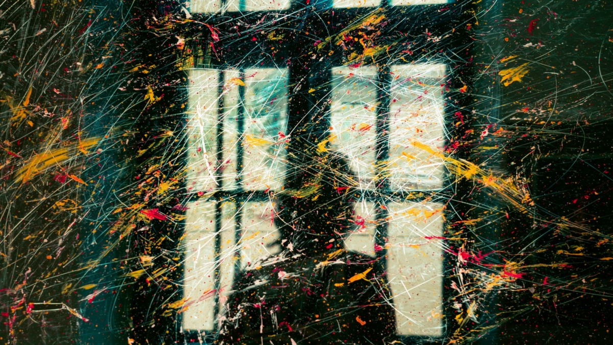 Asilhouette of a person in fron of a window and a transparent glass with paint strokes of different colors overlaying the image