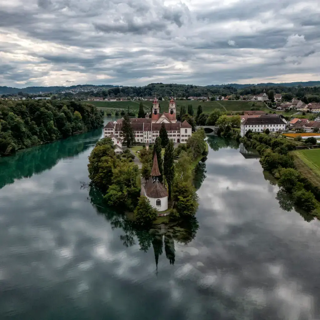 Aerial view of Rheinau Monastery on the Rhine River in Switzerland, surrounded by forests, fields, and water reflections. Landscape Photography. Luftaufnahme des Klosters Rheinau am Rhein in der Schweiz, umgeben von Wäldern, Feldern und Spiegelungen im Wasser. Landschaft Fotografie.