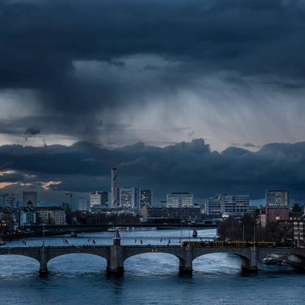 Blue hour storm clouds over Basel skyline and the Rhine River with Mittlere Brücke in the foreground, photographed by Alan Philip Muller. Gewitterwolken zur blauen Stunde über der Basler Skyline und dem Rhein mit der Mittleren Brücke im Vordergrund, fotografiert von Alan Philip Muller.