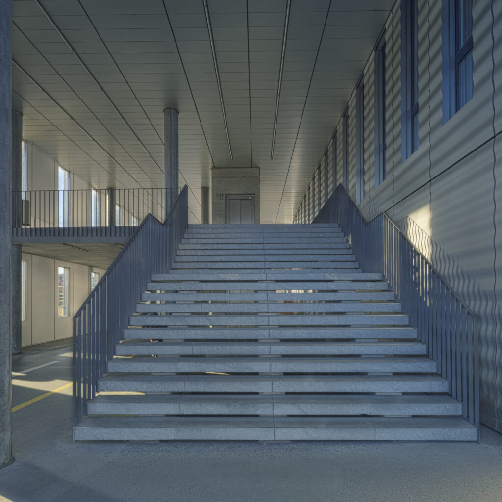 Architecture photography of the Jacob Burckhardt Haus in Basel featuring a central concrete staircase with symmetrical railings and soft daylight. Architekturfotografie des Jacob Burckhardt Haus in Basel mit einer zentralen Betontreppe, symmetrischen Geländern und weichem Tageslicht.