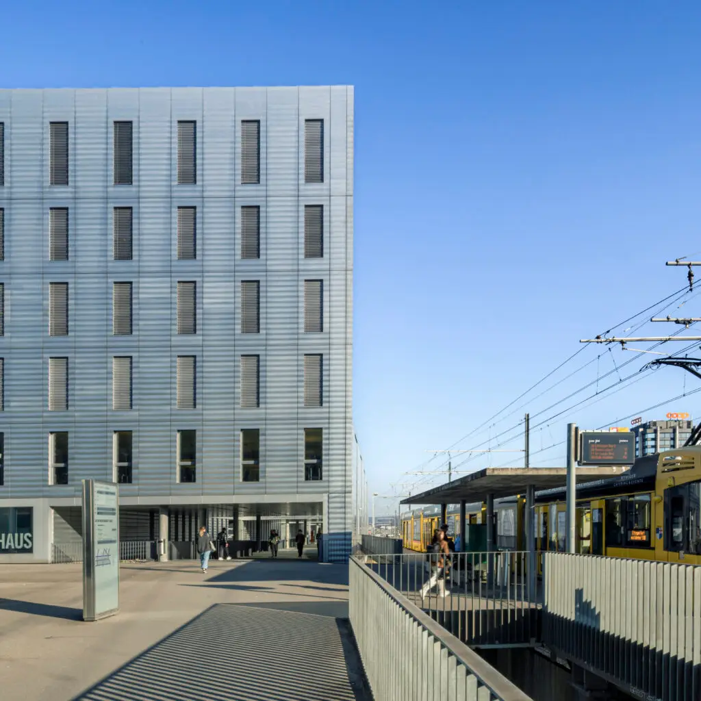 Architecture photography of the Jacob Burckhardt Haus in Basel showing the metal facade, tram platform and people in the public space. Architekturfotografie des Jacob Burckhardt Haus in Basel mit Metallfassade, Tramperron und Menschen im öffentlichen Raum.